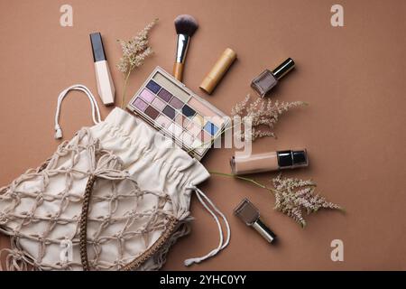 Handgefertigte Makramee-Einkaufstasche mit Make-up-Produkten und Spitzen auf braunem Hintergrund, flach gelegt Stockfoto