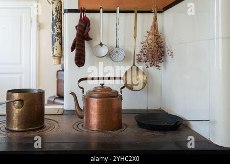 Eine altmodische Kücheneinrichtung. Kupfertopf und Wasserkocher auf dem Holzofen. Set mit alten Küchenutensilien. Stockfoto