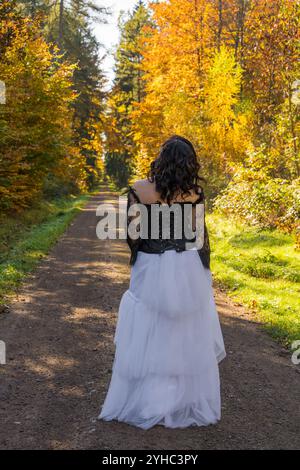 Attraktive Frau in Lederjacke, weißem langen Rock im Herbstwald, der auf einem Pfad die Natur genießt. Stockfoto