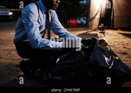 Abgeschnittener Schuss eines schwarzen Polizisten, der am Tatort Leichnam schließt, während er Verbrechen ermittelt Stockfoto