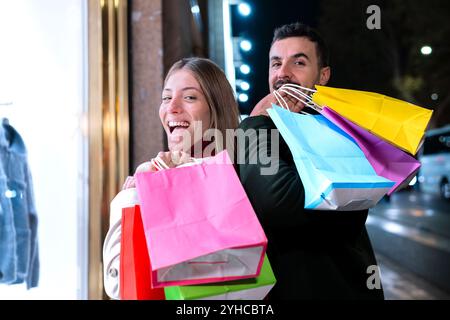 Glückliches Paar genießt Nachteinkäufe mit bunten Taschen in einer urbanen Umgebung Stockfoto