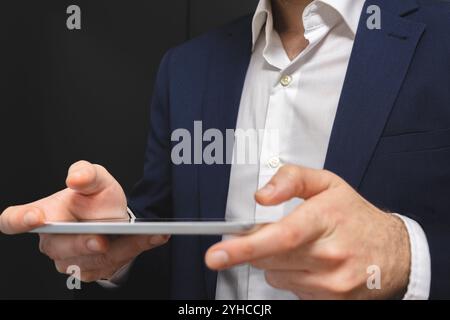 Geschäftsmann mit digitalem Tablet auf schwarzem Hintergrund. Nahaufnahme der männlichen Hände, die das Touchpad halten. Stockfoto