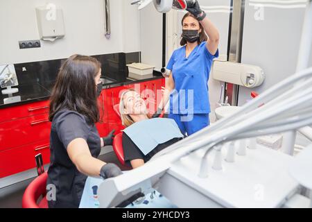 Eine Frau sitzt auf einem Zahnarztstuhl und zwei Frauen stehen hinter ihr. Stockfoto