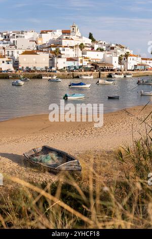 Altes Fischerboot an einem Strand mit dem alten Dorf Ferragudo im Hintergrund, Portugal Stockfoto