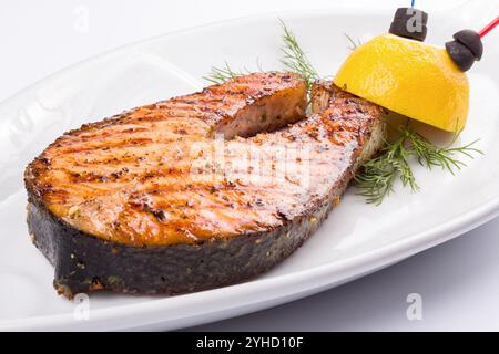 Gegrilltes Fischsteak auf dem weißen Teller, dekoriert mit Zitrone. Großansicht. Einfache gekochte Forelle Stockfoto
