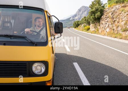 Junger Mann, der seinen gelben Retro-Wohnwagen auf einer bergigen Küstenstraße in Kroatien fährt Stockfoto