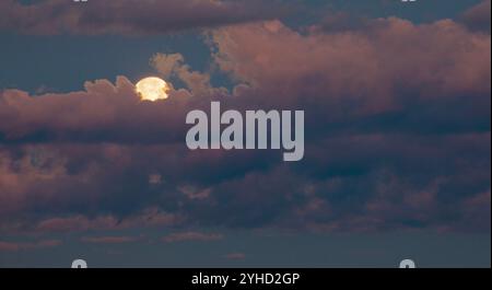 Der Vollmond steigt auf und die Wolken haben noch Farbe, nachdem die Sonne untergegangen ist. Stockfoto