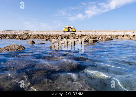 Gelber Retro-Wohnmobil parkt am felsigen wilden Strand auf der Insel Pag, Kroatien Stockfoto