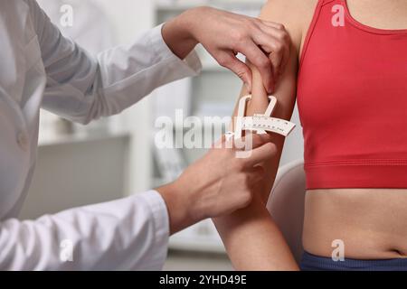 Arzt misst das Körperfett der Frau mit dem Messschieber in der Klinik, Nahaufnahme Stockfoto