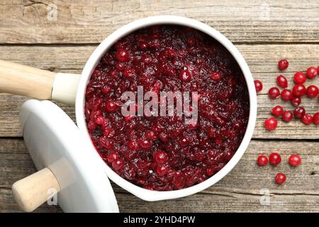 Leckere Preiselbeersauce in einem Topf und Beeren auf Holztisch, Blick von oben Stockfoto