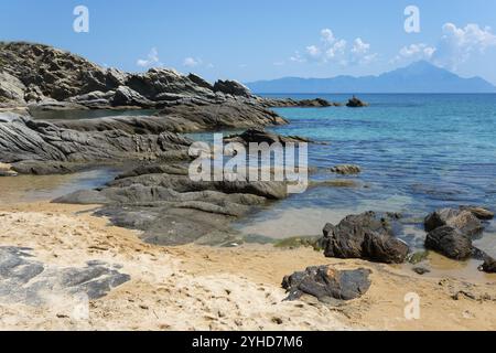 Ruhiger Strand mit Felsen, im Hintergrund das Meer und ferne Berge unter einem klaren Himmel, Blick auf den Berg Athos, Sarti, Sithonia, Chalkidiki, Chalkidiki Stockfoto