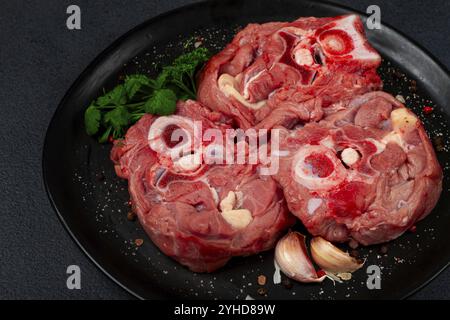 Rohes Steak, Kalbhals auf den Knochen, frisches Fleisch, auf einem schwarzen Teller, Blick von oben, keine Leute Stockfoto