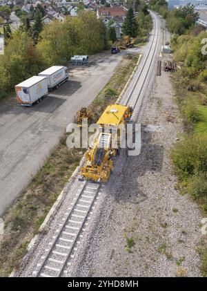 Luftaufnahme einer gelben Baumaschine auf Eisenbahngleisen mit Lastwagen und umliegenden Grünflächen und Häusern, Stanzmaschine, Hermann Hessebahn Stockfoto