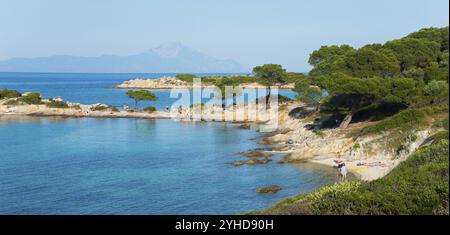 Malerische Küstenlandschaft mit felsigem Strand und Bäumen vor klarem blauem Wasser, Karidi Strand, Karydi, Berg Athos im Hintergrund, Vourvourou Stockfoto