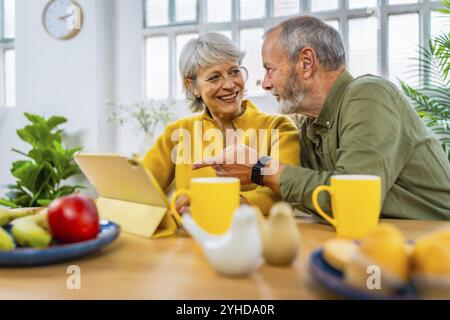 Ein älteres Ehepaar erkundet das Internet mit einem digitalen Tablet zu Hause beim Frühstück Stockfoto