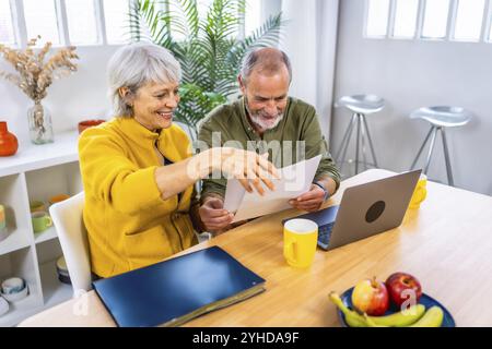 Seniorenpaar, das Rechnungen durchgeht, mit Laptop im Wohnzimmer mit Kaffeetasse Stockfoto