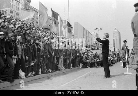 01.05.1980 DDR Ost Berlin Mitte Bezirk. Szene am Rande der Demonstration vom 1. Mai. Eine junge Frau dirigiert einen Chor von Mitgliedern der Pater Stockfoto