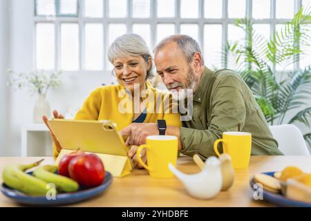 Glückliches weißes modernes Seniorenpaar, das zu Hause mit einem digitalen Tablet im Internet surft Stockfoto