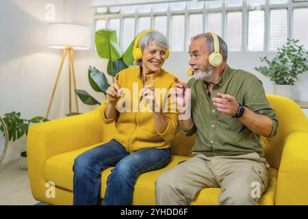 Niedliches Seniorenpaar, das gemeinsam Musik hört und drinnen auf dem Sofa sitzt Stockfoto
