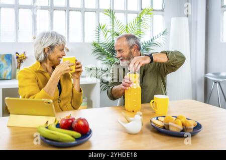 Seniorenpaar genießen gesundes Frühstück zu Hause mit Tablet und sprechen zusammen Stockfoto