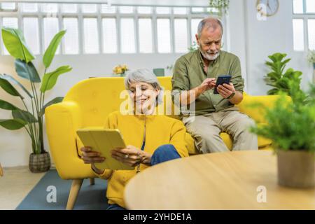 Seniorenpaar, die zu Hause verschiedene Geräte und Technologien gemeinsam nutzen Stockfoto