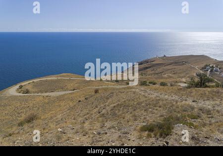 Panorama eines Berges an der Küste mit einer kurvenreichen Schotterstraße, die zum Leuchtturm führt. Kap Meganom, Krim, ein sonniger Tag im September Stockfoto