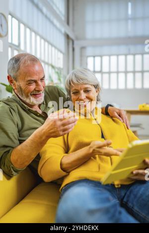 Seniorenpaar liest gemeinsam Online-Nachrichten auf dem Sofa mit einem digitalen Tablet Stockfoto