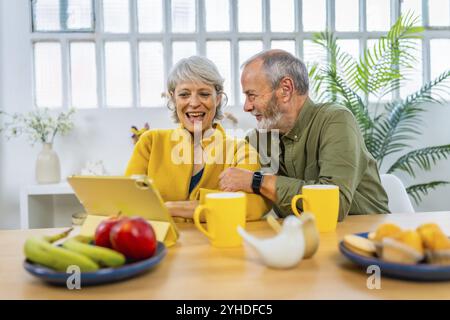 Glückliches Seniorenpaar mit digitalem Tablet zu Hause beim gesunden Frühstück Stockfoto