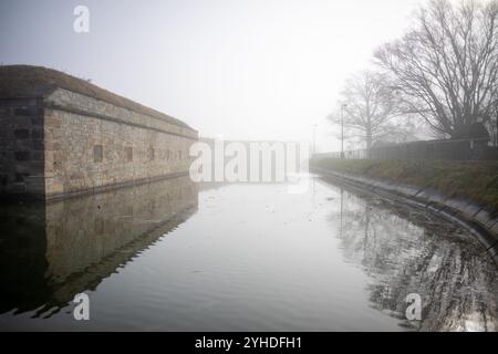 HAMPTON, Virginia – der historische Burggraben und die äußeren Befestigungen von Fort Monroe, Amerikas größtem Steinfort, tauchen durch den Morgennebel auf. Die atmosphärischen Bedingungen betonen die massiven Granitmauern und Verteidigungsmerkmale dieser Küstenbefestigung aus dem 19. Jahrhundert. Dieses erhaltene militärische Meisterwerk zeigt eine anspruchsvolle Küstenverteidigungsarchitektur. Stockfoto