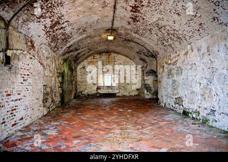 Gewölbtes Kasematteninnere im Fort Monroe Virginia | HAMPTON, Virginia — Eine gewölbte Ziegelkasematte öffnet sich zu einem vergitterten Fenster innerhalb der massiven Mauern von Fort Monroe. Diese Kammern, die zwischen 1819 und 1834 gebaut wurden, um Artilleriemannschaften und Kanonen hinter zehn Fuß dicken Mauerwerken zu schützen, beherbergten später einen ganz anderen Insassen: Der konföderierte Präsident Jefferson Davis wurde hier in einer fast identischen Kasematte nach seiner Gefangennahme im Jahr 1865 festgehalten. Stockfoto