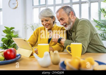 Glückliches verheiratetes Seniorenpaar, das gemeinsam ein Tablet benutzt, während es zu Hause frühstückt Stockfoto