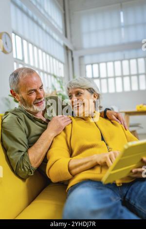 Vertikales Foto eines modernen Seniorenpaares, das sich zu Hause entspannt und zusammen ein digitales Tablet verwendet Stockfoto