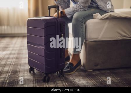 Nahaufnahme des Reisekoffers und des Reisenden, der auf dem Bett im Hotelzimmer sitzt. Stockfoto