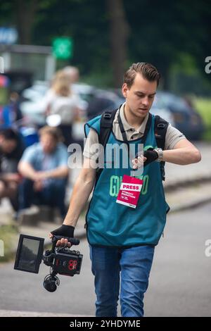 Utrecht, Region Utrecht, Niederlande - 19.05.2024: Ein junger Pressefotograf mit blauer Weste und rotem „Press“-Abzeichen geht, während er seine Wri überprüft Stockfoto