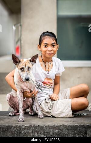 Ein wunderschönes, junges philippinisches Mädchen posiert und lächelt mit ihrem Hund, der vielleicht ein streunender Hund sein könnte, Rizal Park, Manila, die Philippinen. Stockfoto