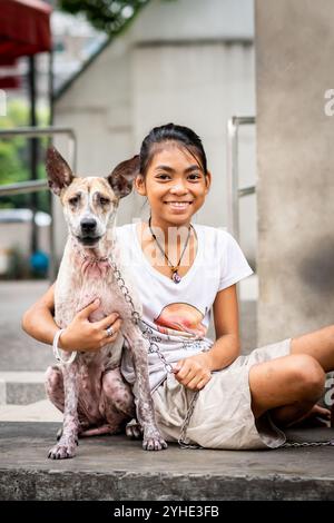 Ein wunderschönes, junges philippinisches Mädchen posiert und lächelt mit ihrem Hund, der vielleicht ein streunender Hund sein könnte, Rizal Park, Manila, die Philippinen. Stockfoto