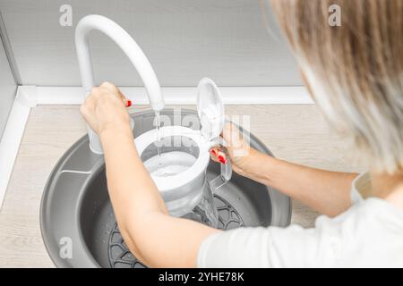 Hausfrau gießt Wasser in den Wasserfilter in der Küche. Frau füllt Wasserfilter in Küchenspüle. Hausfrau mit Maniküre. Hochwertige Fotos Stockfoto