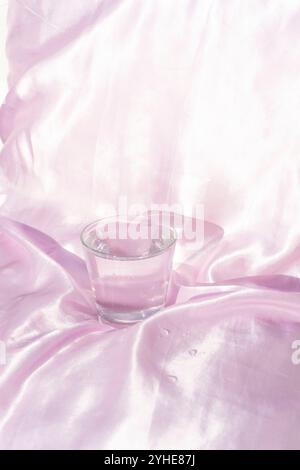 Elegantes Glas Wasser auf weichem rosa Stoffhintergrund Stockfoto