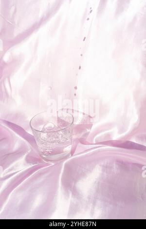 Erfrischendes Glas Wasser auf rosa Seidenstoff mit Wassertropfen Stockfoto