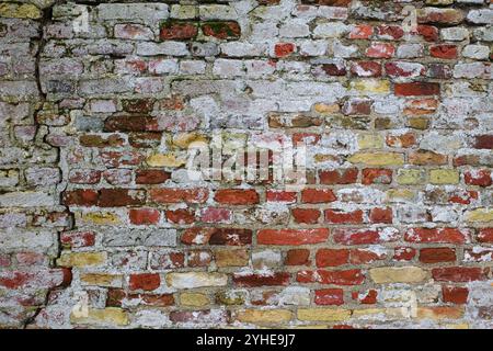 Sehr alte rustikale Mauer mit gelben und roten Ziegeln. Es gibt einen Riss in der Wand. Reste weißer Farbe sind sichtbar Stockfoto