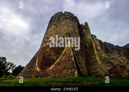 Blick auf einen der massiven runden Türme in der äußeren Burgmauer von Chepstow Castle in Wales, der bis zu einem unheilvollen stürmischen Himmel reicht Stockfoto