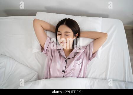 Eine ruhige und sanfte Szene einer Frau in ihrem Schlafzimmer, die sich in den frühen Morgenstunden friedlich im Bett liegend und die Schönheit der Entspannung zeigt Stockfoto