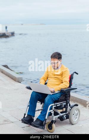 Mann mit Behinderungen, der im Rollstuhl sitzt und an einem Laptop arbeitet Stockfoto