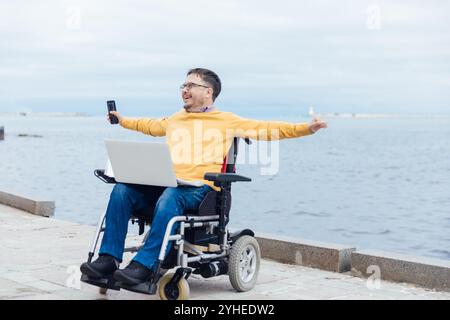 Ein Mann sitzt in einem Rollstuhl auf einem Spaziergang durch die Stadt und freut sich in seinen Händen zur Seite Stockfoto