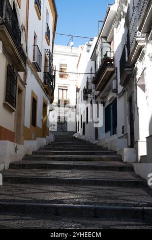 Ein schmaler Fußweg, flankiert von traditionellen Gebäuden mit Balkonen, führt durch eine charmante Gasse in Cordoba, die einen friedlichen Durchgang freigibt Stockfoto