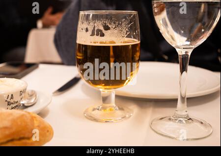 Ein erfrischendes Glas Bier liegt auf einem Esstisch vor einem leeren Teller Stockfoto