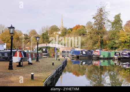 Braunston, Northamptonshire, Großbritannien, 2024: Farbenfrohe Schmalboote liegen im Yachthafen mit alten Laternenpfosten an der Kai und herbstlichen Bäumen dahinter. Stockfoto