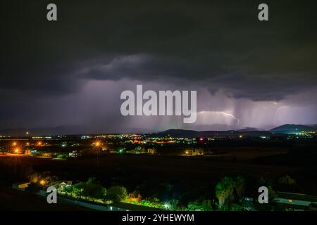 Helle Blitze ziehen über die Wolken und enthüllen eine pulsierende Stadt unter einem stürmischen Himmel. Stockfoto