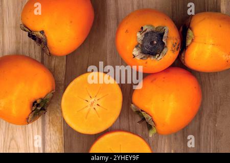 Blick von oben auf frische organische Persimmonen auf hölzernem Hintergrund, halbierte orange Persimmon Früchte von Rojo brillante Sorte Stockfoto