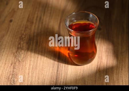 Ein mit Bernsteintee gefülltes Glas liegt auf natürlichem Holz und leuchtet sanft im warmen Licht der Nachmittagssonne. Stockfoto